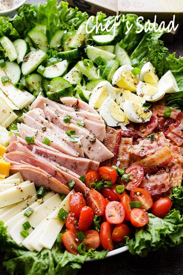 Fresh salad, veggies, eggs, deli meats, and cheese, on a round salad platter.