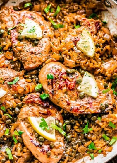 A top view of Chicken Piccata and Rice in a pan with capers, parsley, and sliced lemon