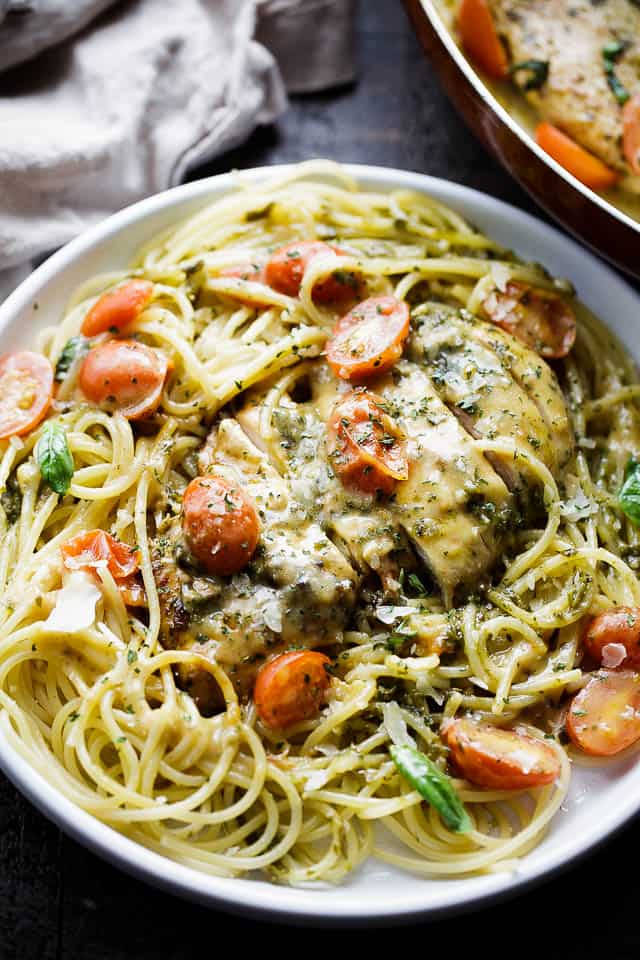 Sliced chicken served over a plate of spaghetti with cherry tomatoes mixed in.