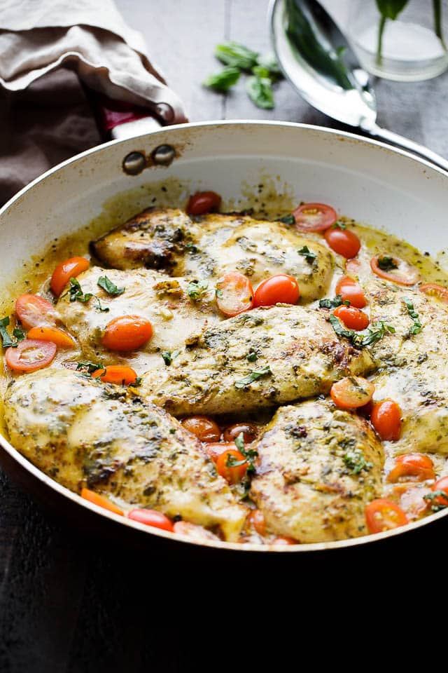 Four cooked chicken breasts in a sauce with halved cherry tomatoes.