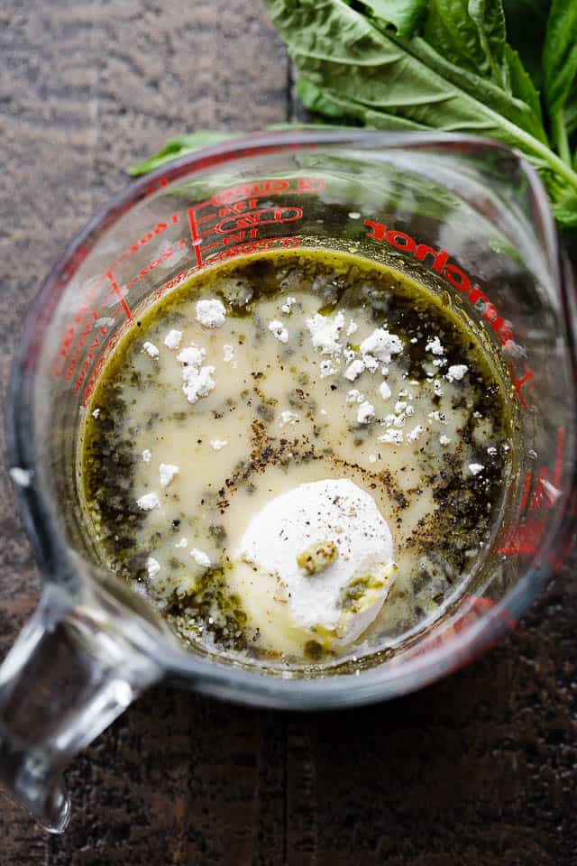 A measuring cup with basil pesto, evaporated milk, and flour.