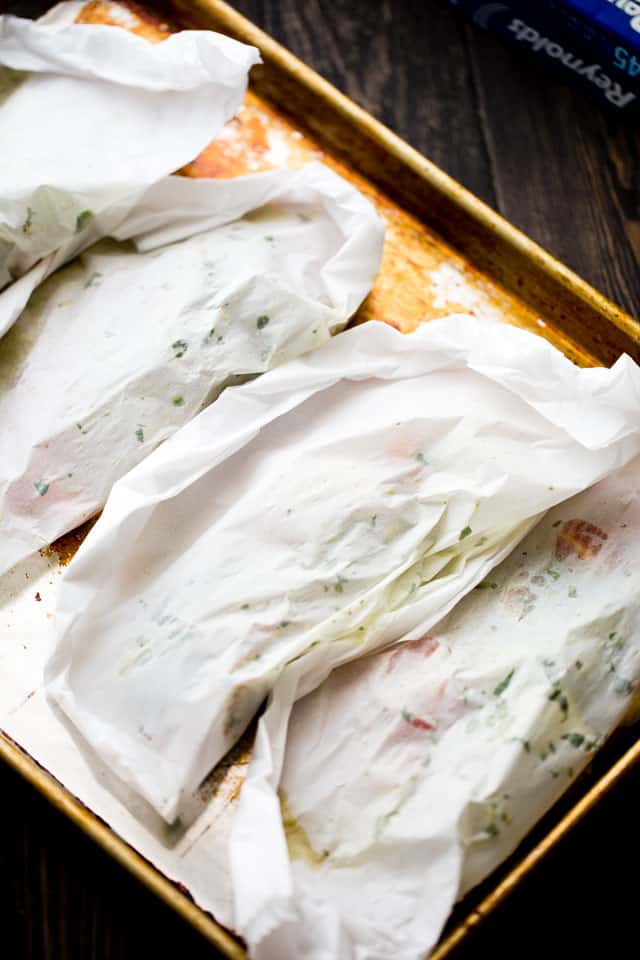 Four parchment packets with shrimp arranged on a rimmed baking sheet.