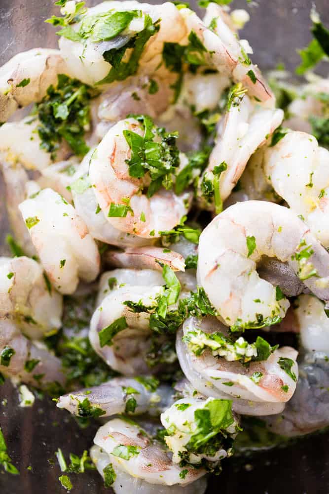 Shrimp sitting in a marinade with parsley, lemon juice, and garlic.