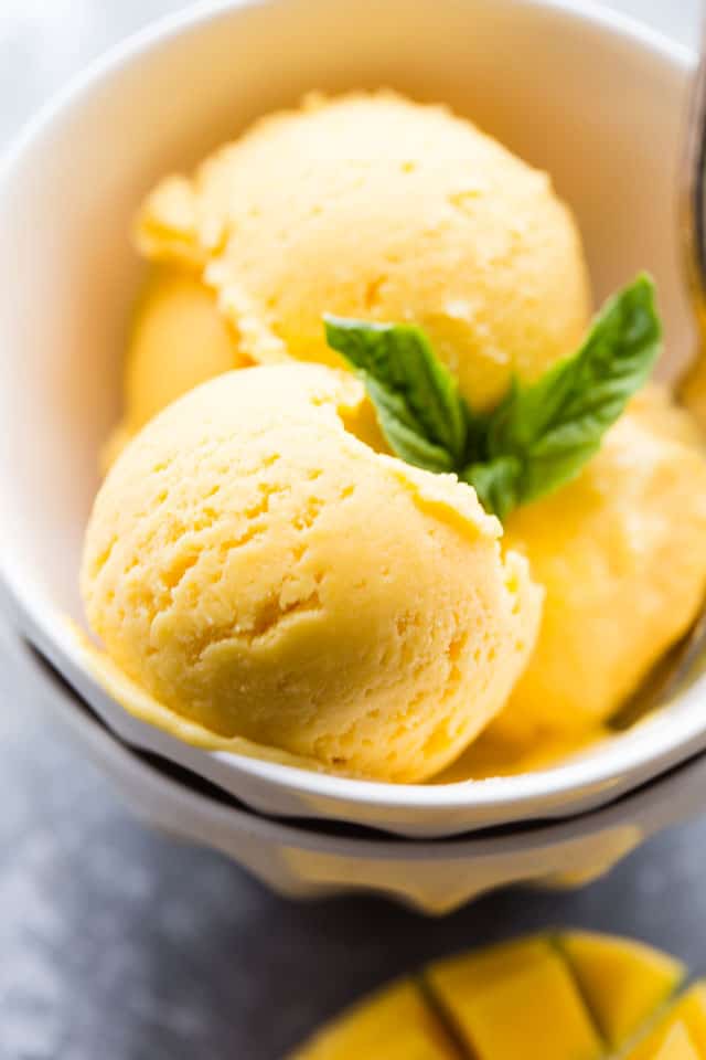 Close-up shot of three mango sorbet balls in a white bowl.