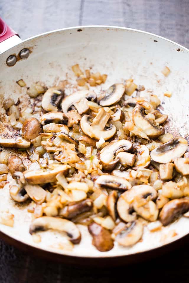 Sliced mushrooms sauteeing in a skillet.