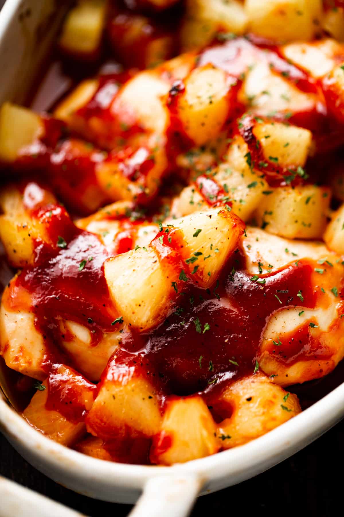 raw chicken breasts in an oval dish, topped with pineapple chunks and bbq sauce.