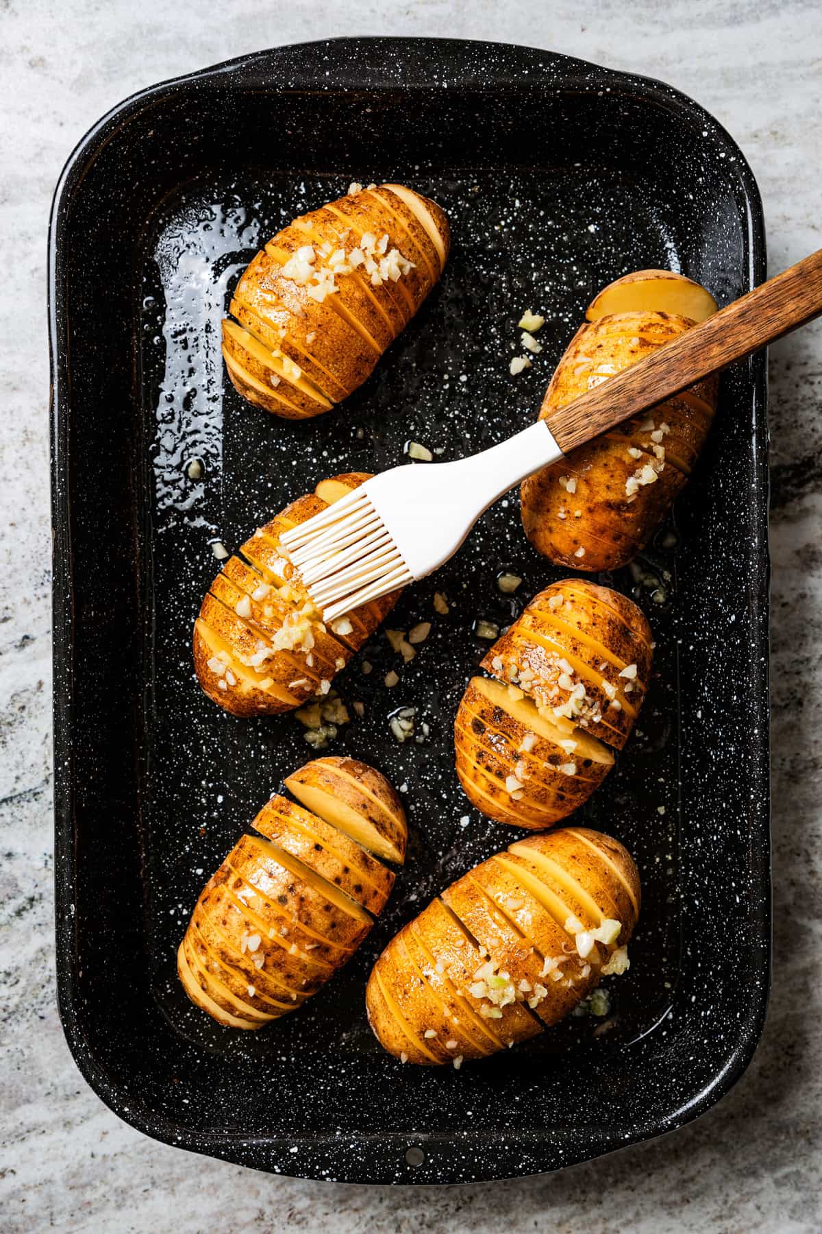 Brushing garlic butter over fanned potatoes with a pastry brush.