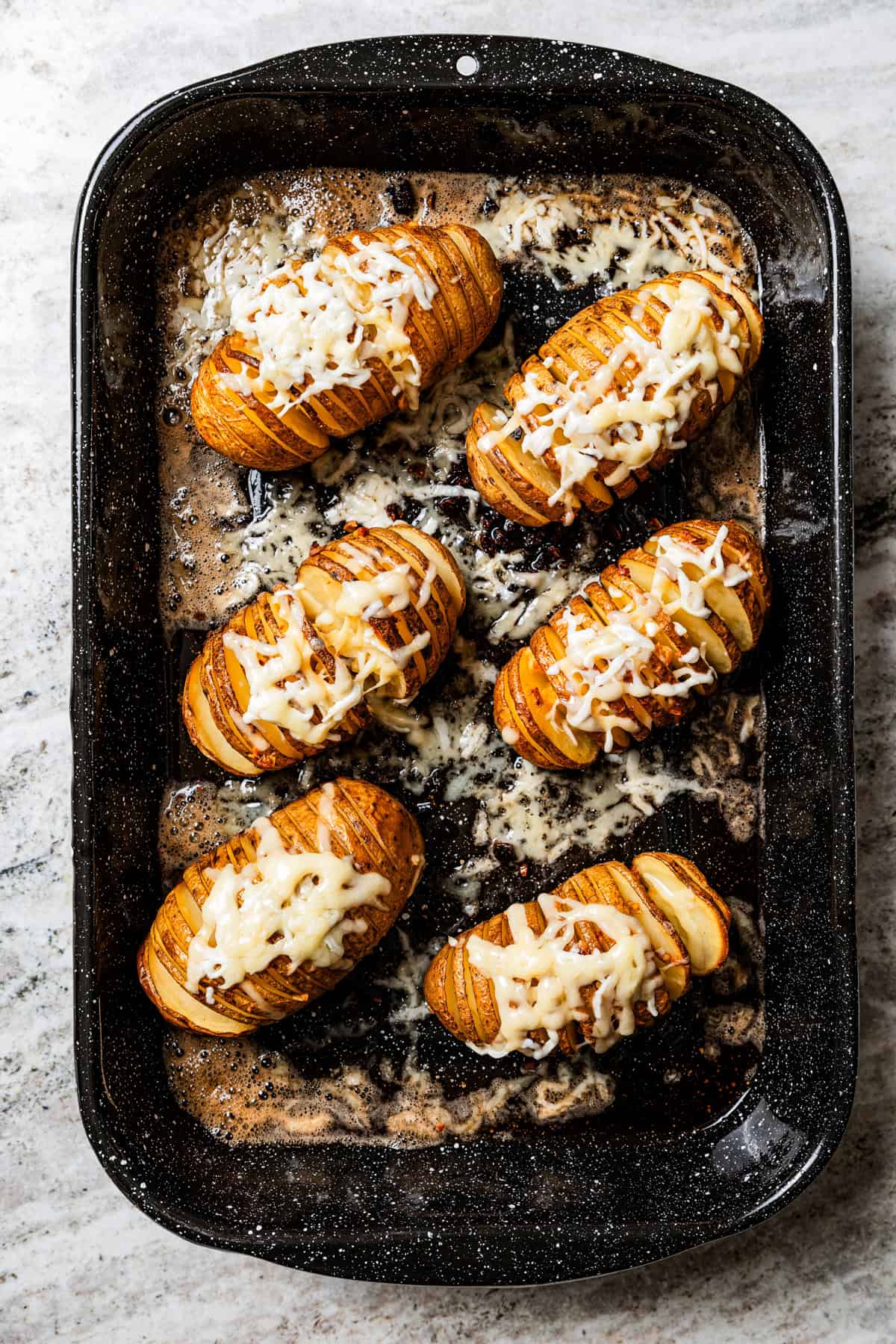 Overhead view of hasselback potatoes topped with shredded parmesan cheese in baking pan.