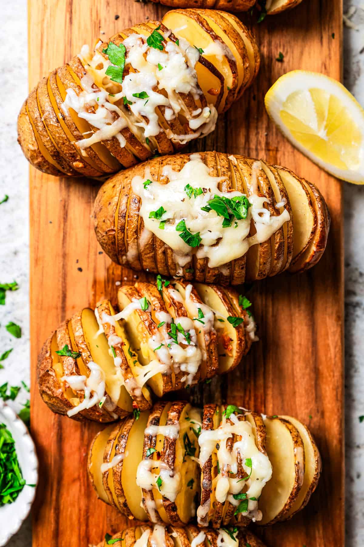 Hasselback potatoes topped with melty cheese are arranged on a wooden cutting board.