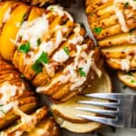 A fork pulling apart a hasselback potato topped with melted cheese.