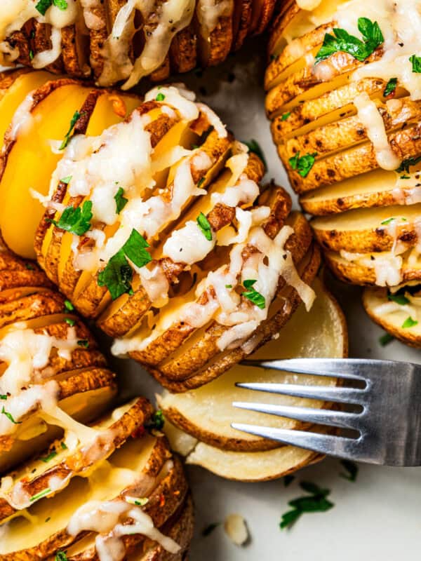 A fork pulling apart a hasselback potato topped with melted cheese.