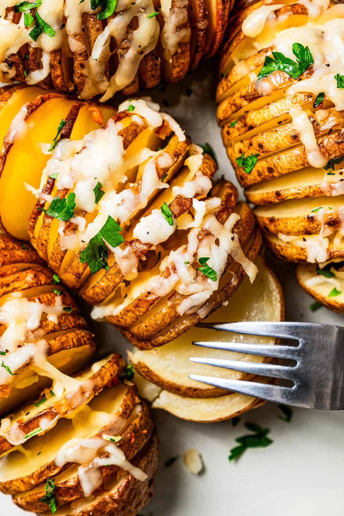 A fork pulling apart a hasselback potato topped with melted cheese.