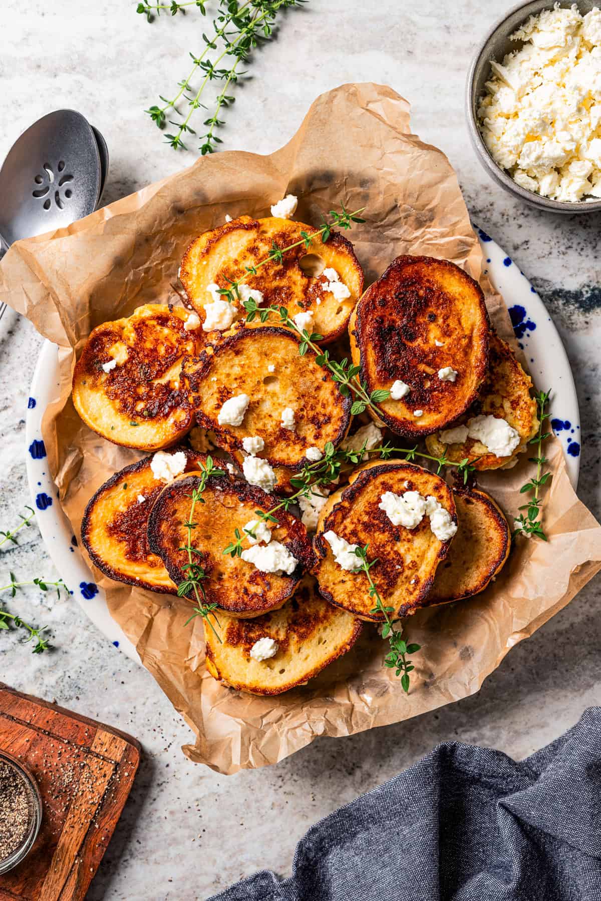 Slices of French toast topped with crumbled feta and thyme and served on a parchment-lined platter.