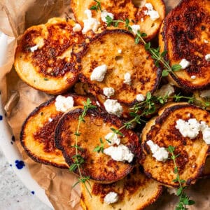 Slices of French toast topped with crumbled feta and thyme and served on a parchment-lined platter.