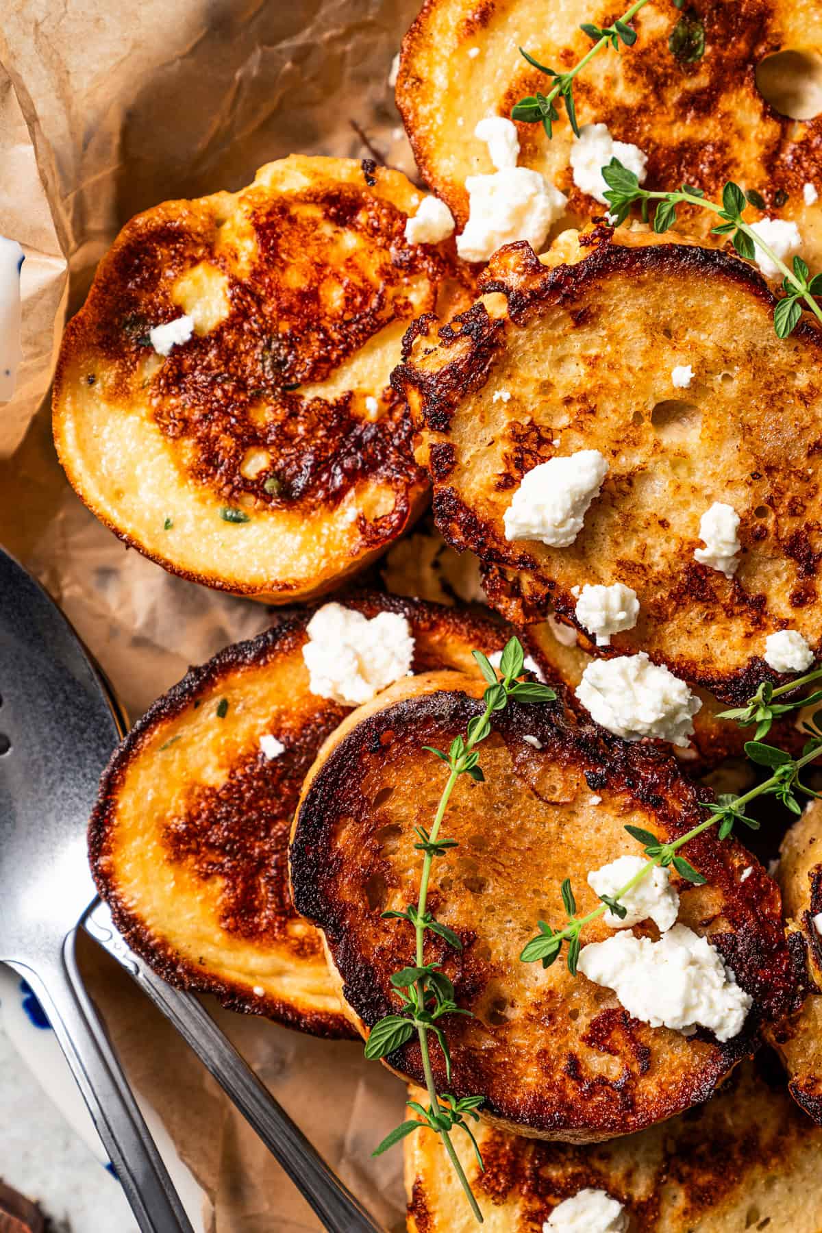 Close-up of savory French toast slices topped with crumbled feta and thyme and served on a parchment-lined platter.