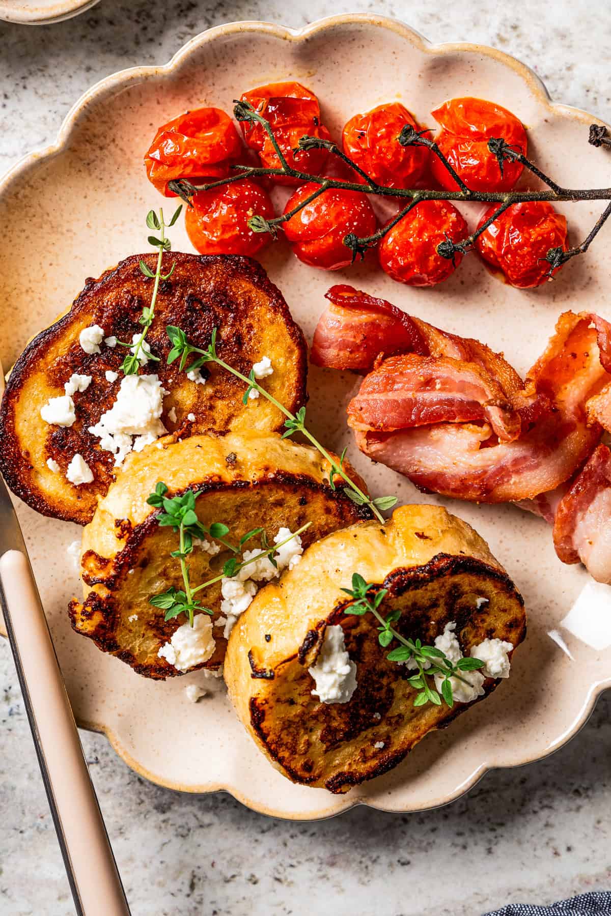 Savory French toast slices served with a side of vine tomatoes and crispy bacon on a plate.