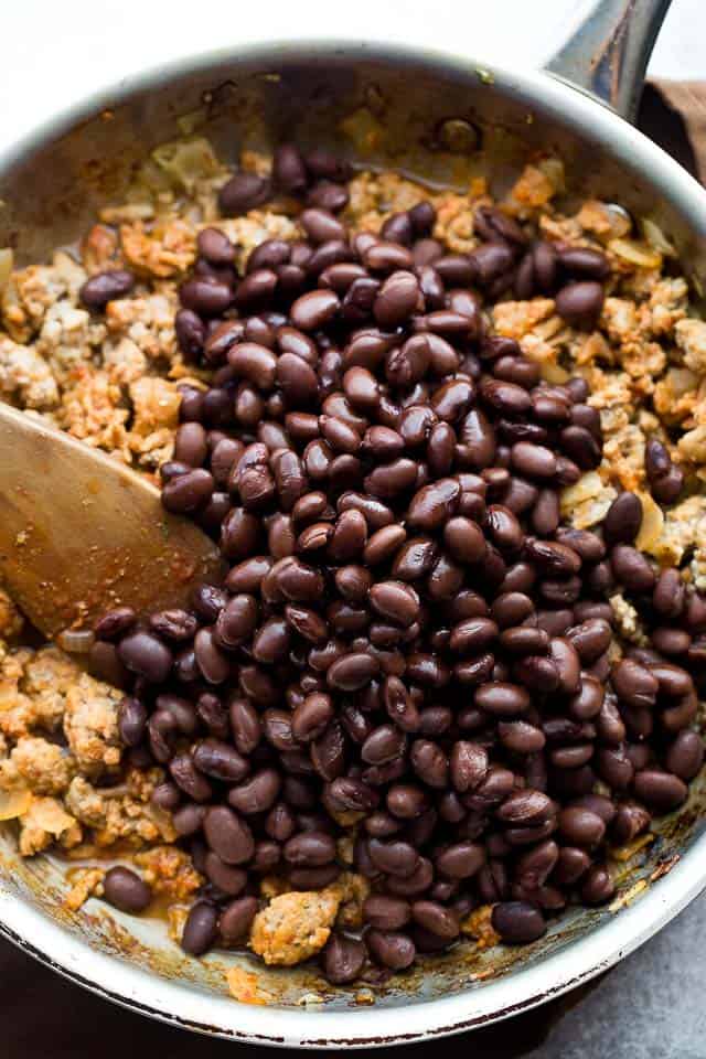 Mixing black beans into a ground turkey mixture in a skillet.