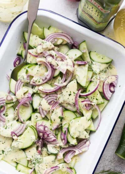 A white dish with a cucumber salad and red onions.