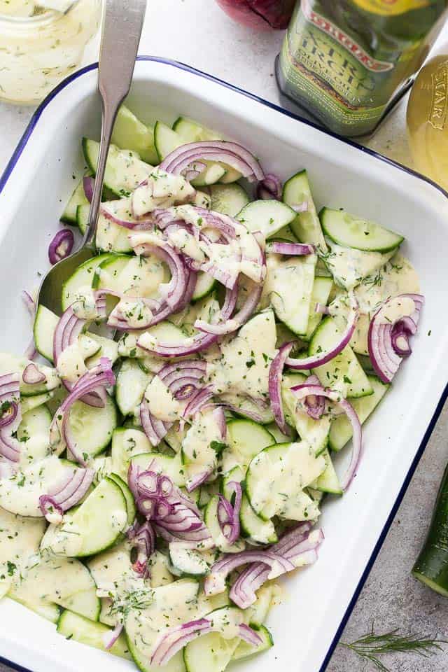 A white dish with a cucumber salad and red onions.