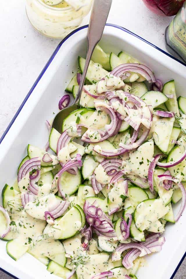 This creamy cucumber salad is a light and refreshing side salad with crisp cucumbers and red onions tossed in herby homemade dressing. Creamy cucumber salad in a white serving dish.
