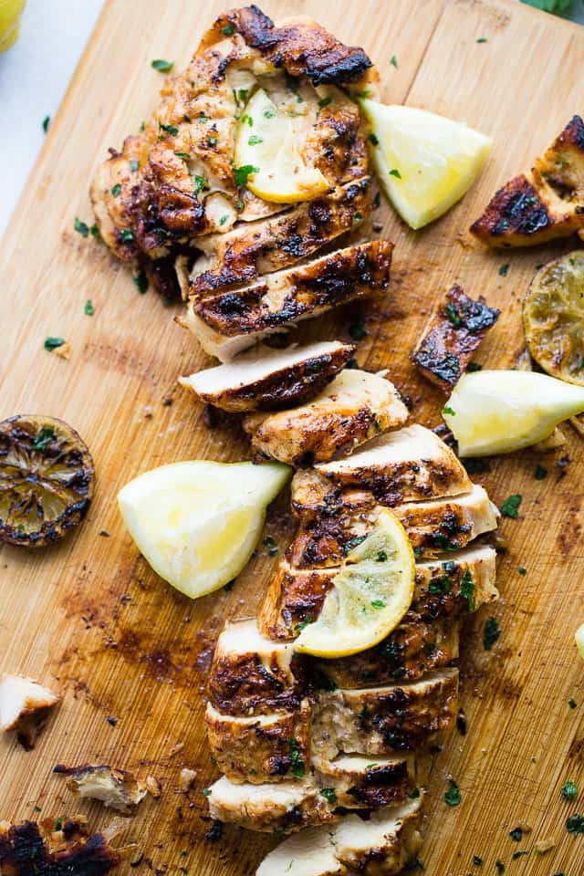 Sliced grilled lemon chicken breast on a cutting board with lemon slices arranged around it.