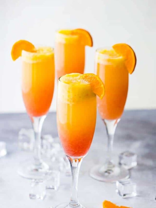 Sunrise mimosa served in four champagne flutes and garnished with orange slices.