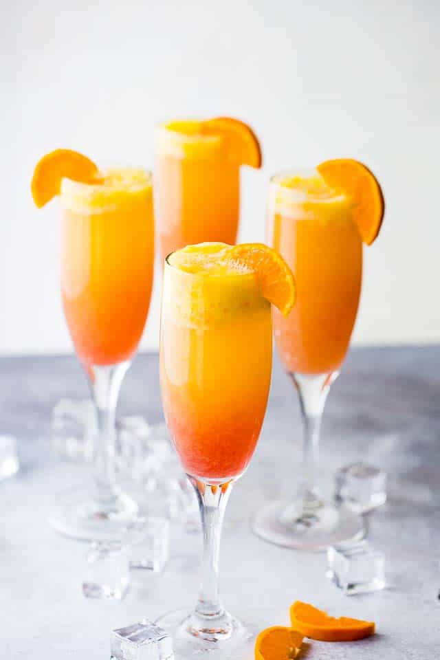 Sunrise mimosa served in four champagne flutes and garnished with orange slices.