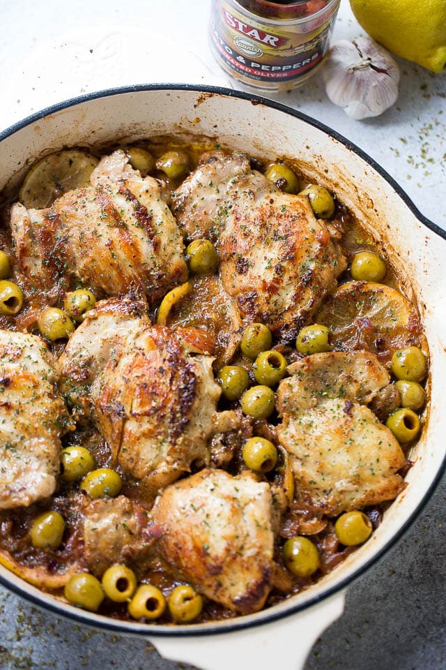 A skillet with chicken thighs, green olives, and lemon slices.