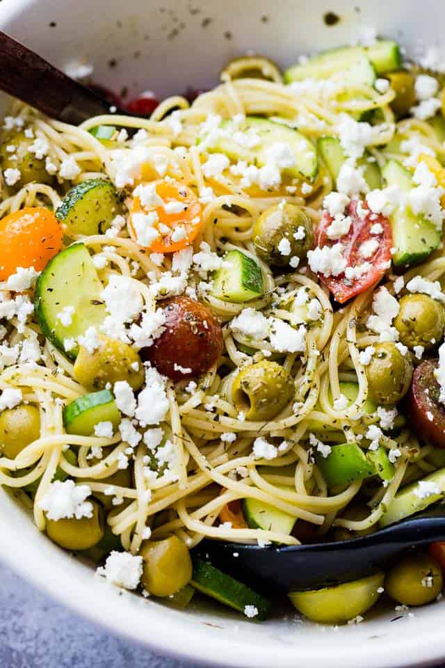 Close-up of cooked spaghetti noodles tossed with sliced cucumbers, olives, chopped tomatoes, and feta cheese.