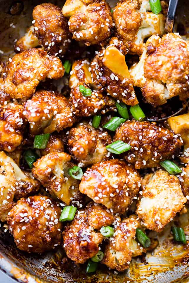 Overhead shot of Cauliflower Bites tossed in a prepared sticky sauce and garnished with white sesame seeds and sliced green onions.