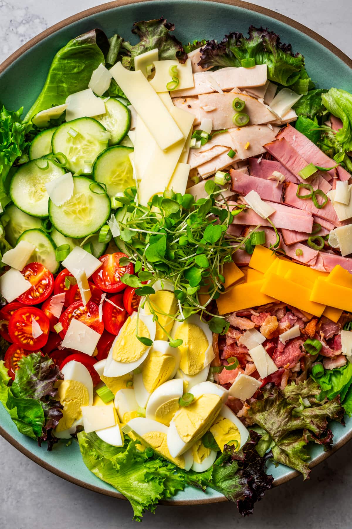 Close up of chef salad ingredients arranged over top of a large bowl of greens.