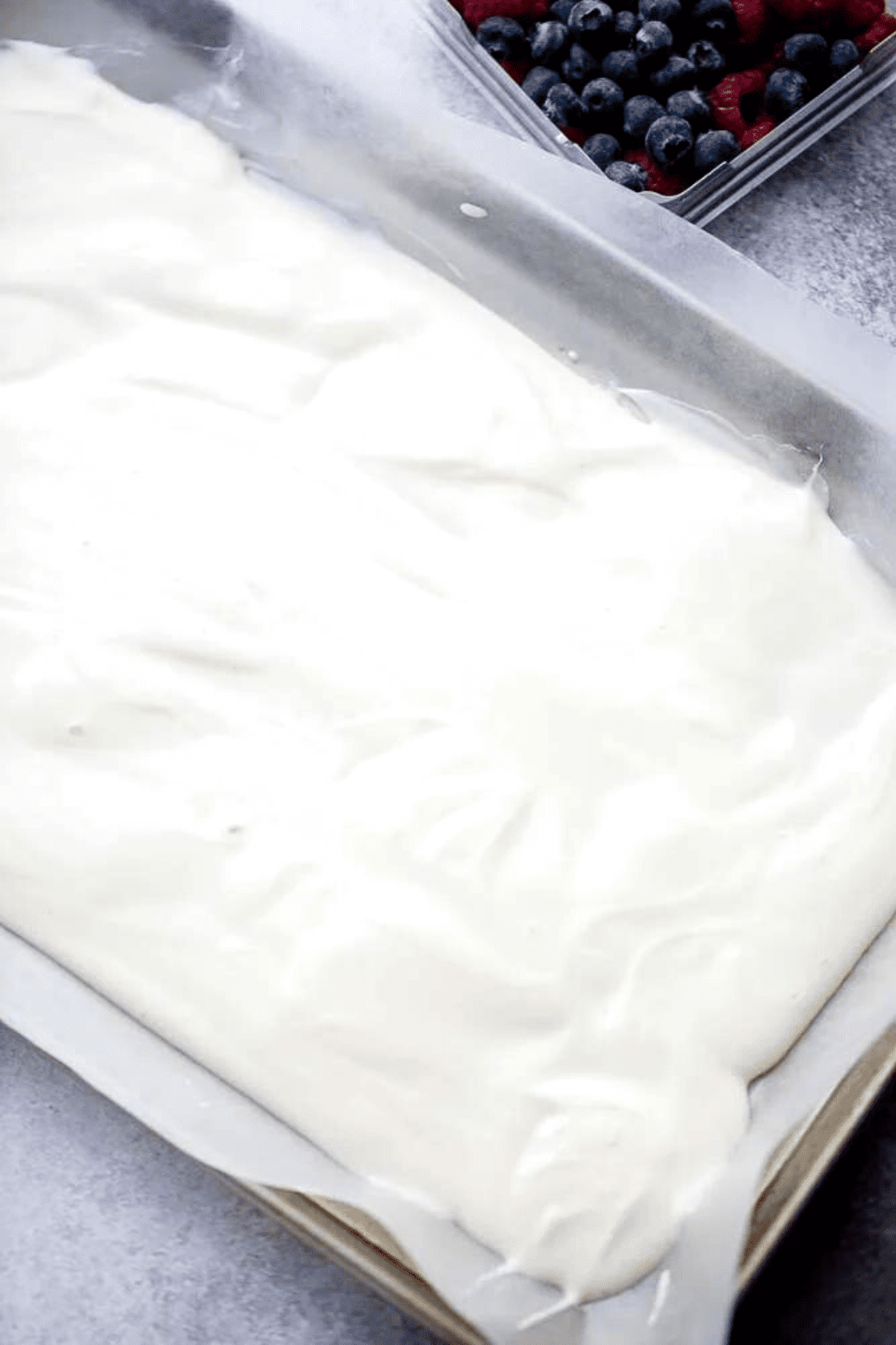 Spreading out a yogurt mixture over a paper-lined baking sheet.