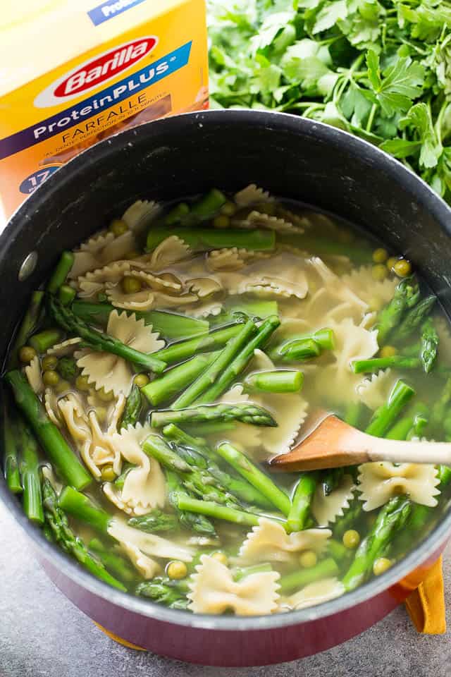 Bow tie pasta with asparagus in a pot of broth.