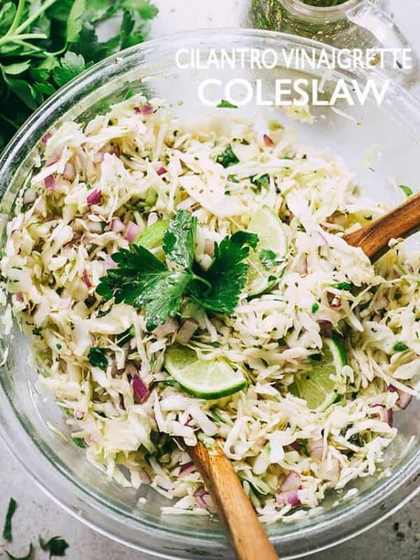 Coleslaw served in a glass mixing bowl with two wooden spoons stirring through it.