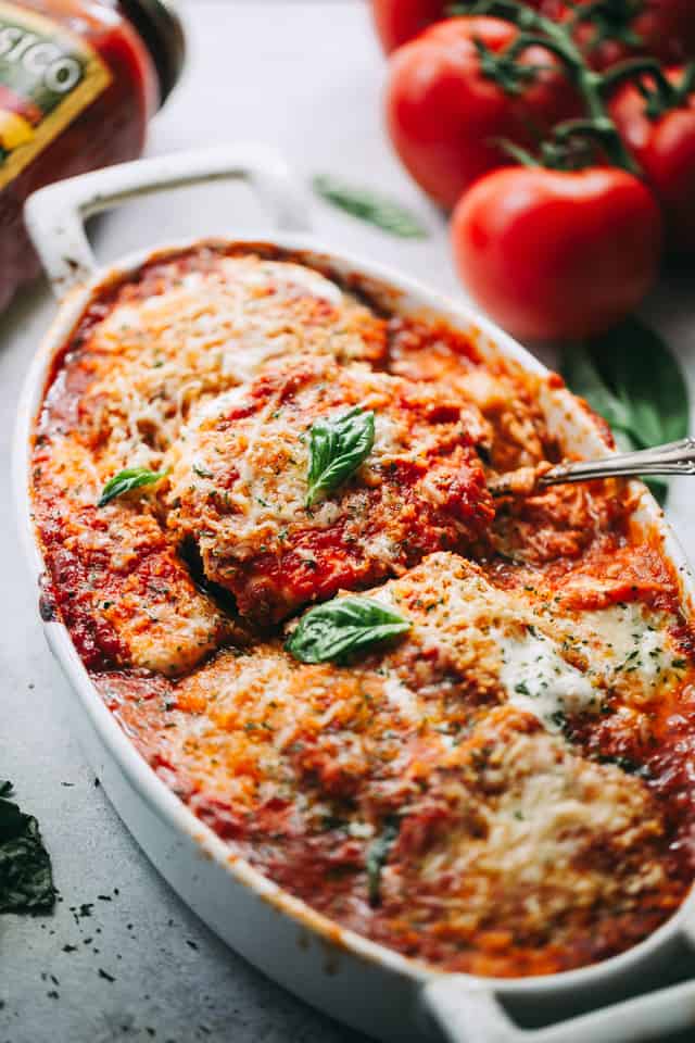 Scooping out cheesy eggplants, with tomatoes placed to one side and a tomato sauce jar on the other.