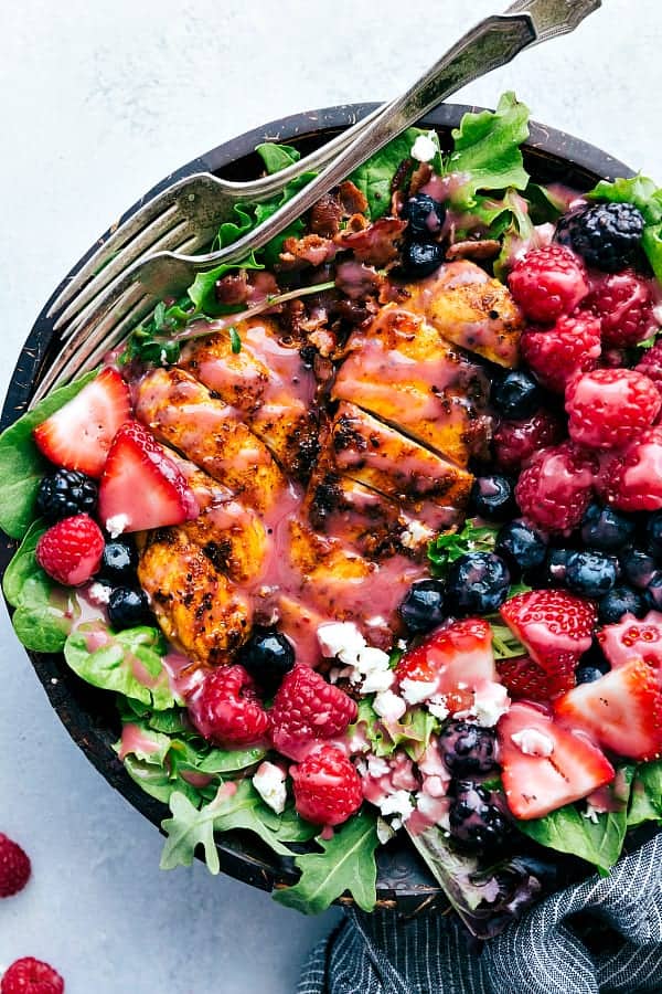 Top view of a green salad topped with grilled chicken, berries and feta