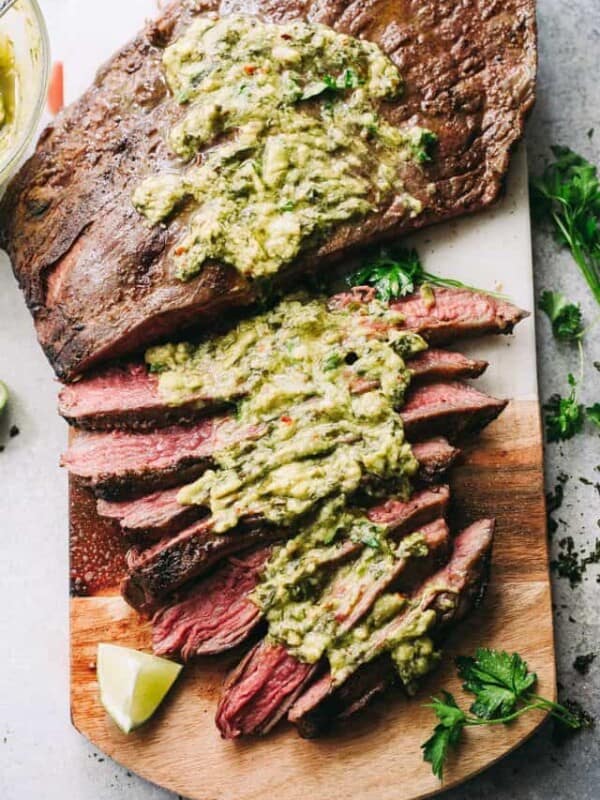 Grilled flank steak with chimichurri sauce on a cutting board.