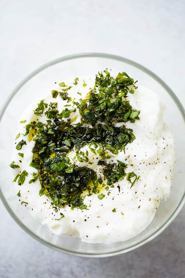 A bowl of yogurt dip garnished with chopped mint.