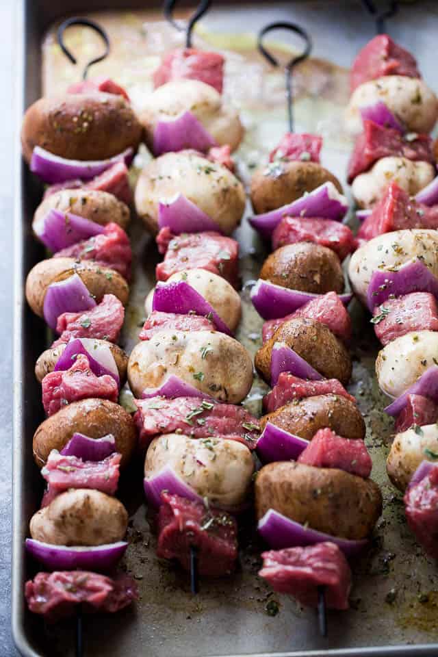 Steak pieces, red onion slices, and mushrooms threaded onto metal skewers.