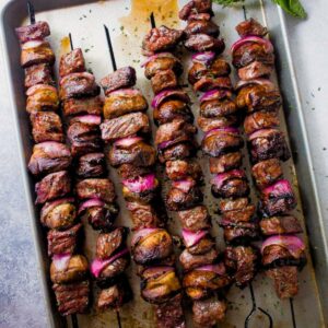 Steak kabobs threaded onto metal skewers and arranged on a rimmed baking sheet.