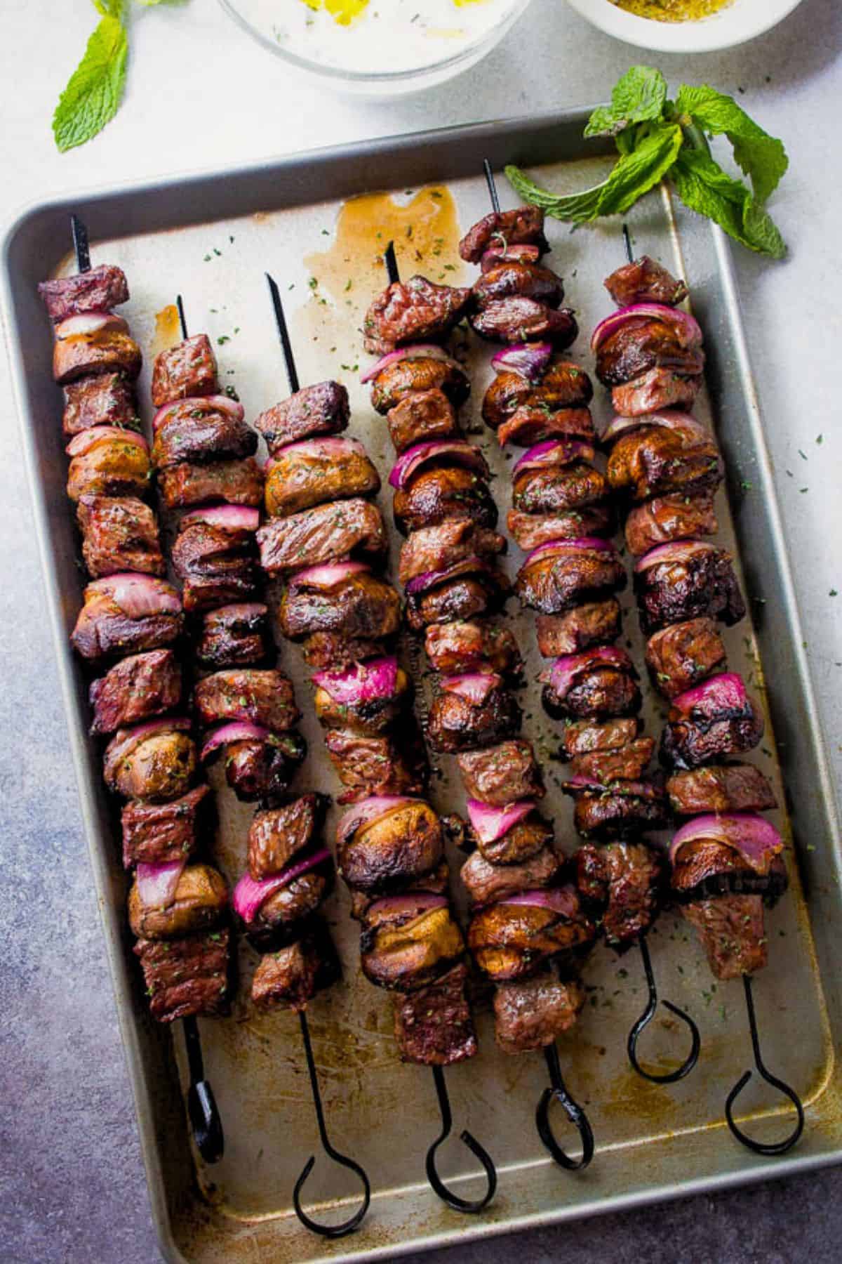 Steak kabobs threaded onto metal skewers and arranged on a rimmed baking sheet.