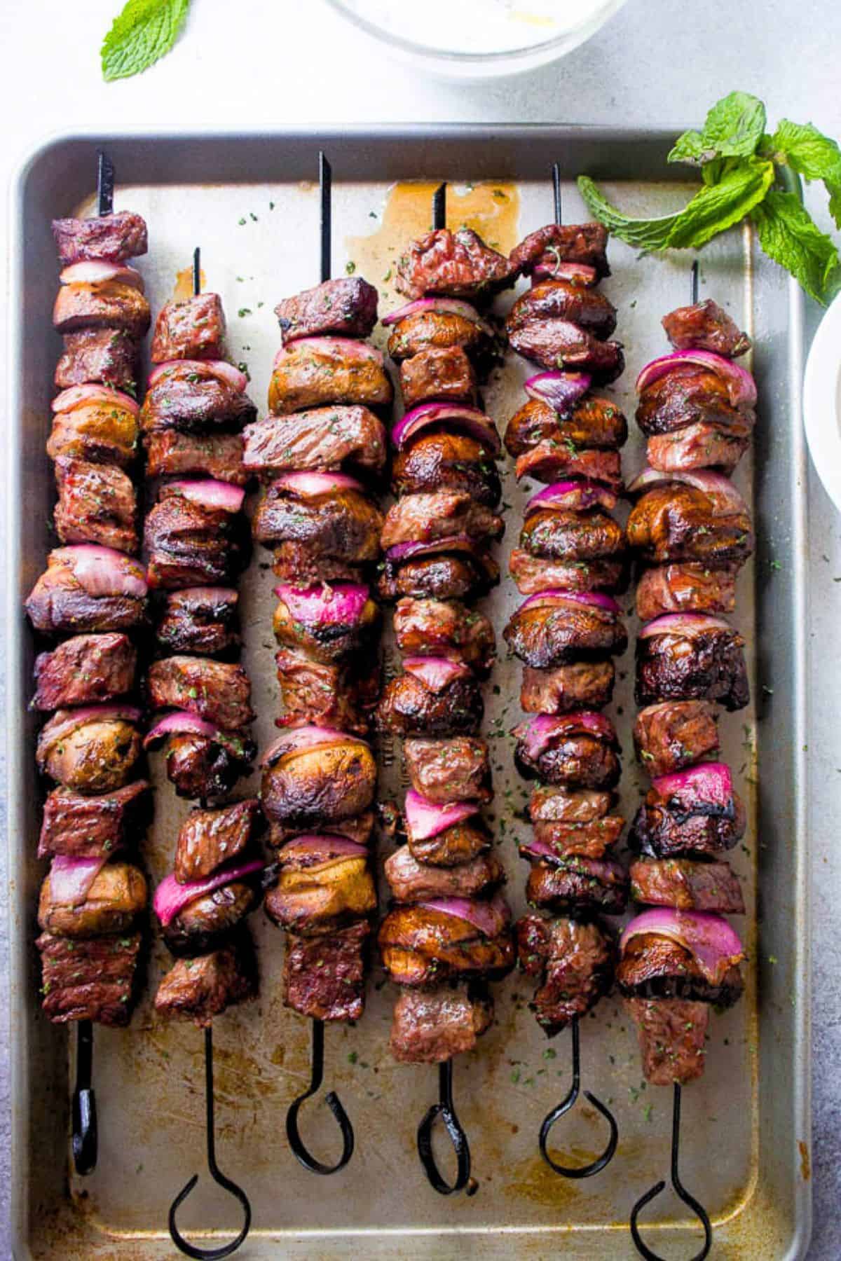 Steak kabobs threaded onto metal skewers and arranged on a rimmed baking sheet.
