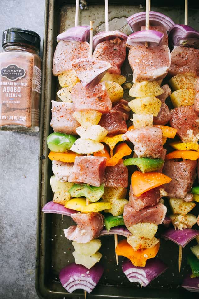 Pork, pineapple pieces and assorted vegetables stacked on a row of skewers and dusted with adobo seasoning.