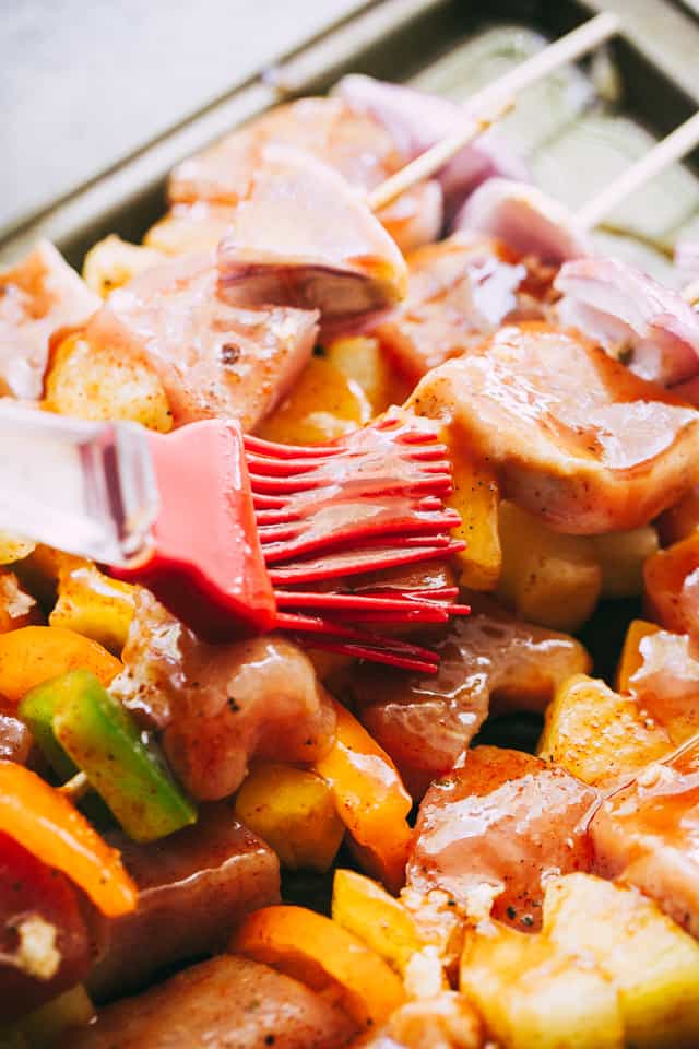 Barbecue sauce being brushed onto a row of pork kebabs.