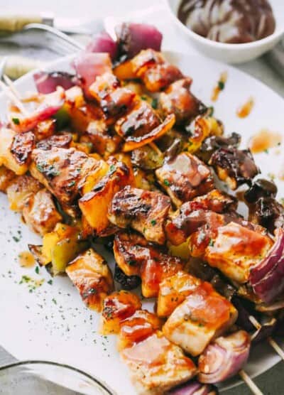 Pineapple BBQ Pork Kebabs stacked on a plate next to a small bowl of extra homemade barbecue sauce.