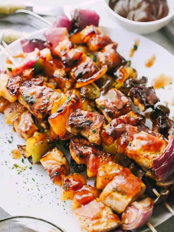 Pineapple BBQ Pork Kebabs stacked on a plate next to a small bowl of extra homemade barbecue sauce.