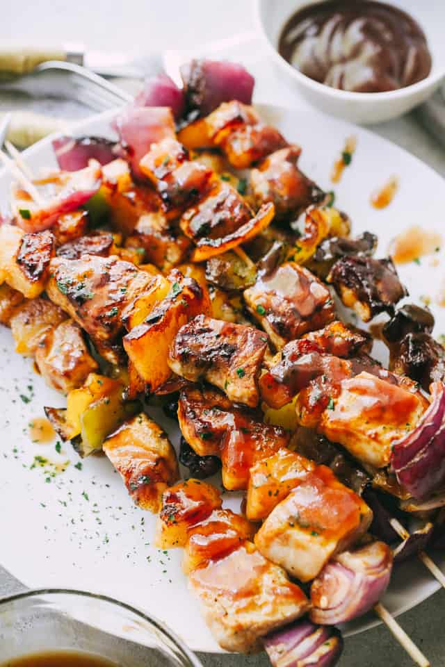 Pineapple BBQ Pork Kebabs stacked on a plate next to a small bowl of extra homemade barbecue sauce.