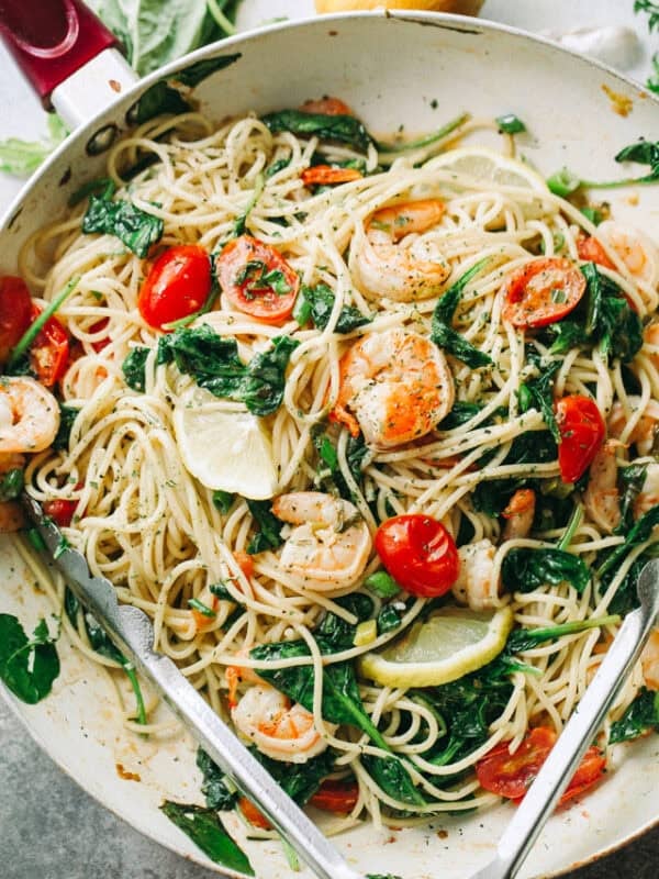 Lemon shrimp spaghetti with sautéed shrimp, spinach, tomatoes, basil, and lemon wedges in a skillet.