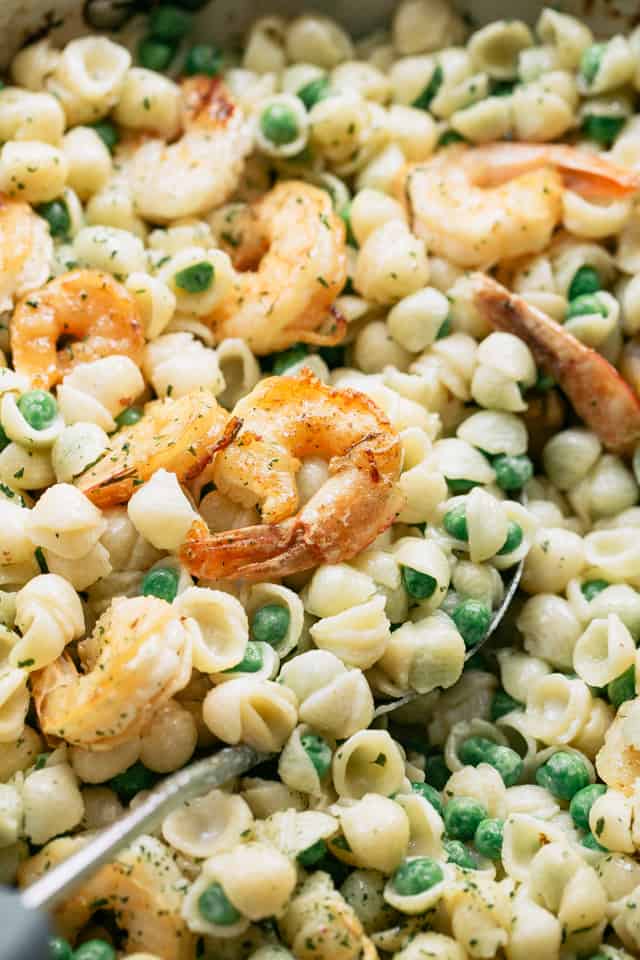 Close-up shot of pasta shells, English peas, and shrimp in a creamy sauce.