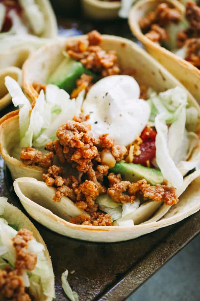 Close-up of Taco Bowls filled with taco-seasoned ground turkey meat, salad, tomatoes, cheese, and topped with a dollop of sour cream